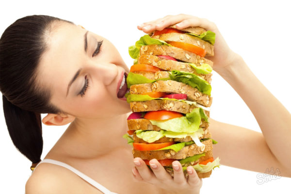 Молодая женщина жадно ест большой бутерброд с овощами и хлебом