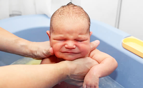 Очень серьёзного младенца купают в ванне