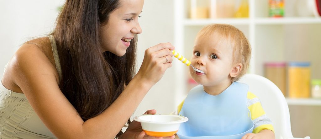 Молодая мама кормит ребенка с ложечки