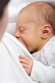 Новорождённый на жёлтом одеяле, на котором сидит медсестра